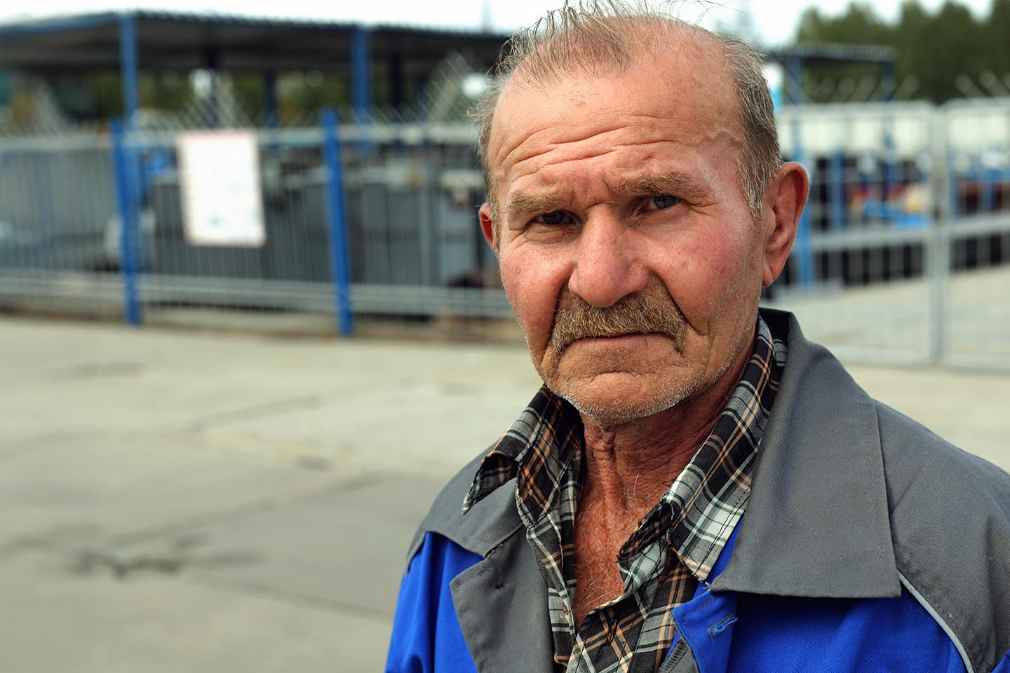 Photo of man in blue and grey standing in front of a fence