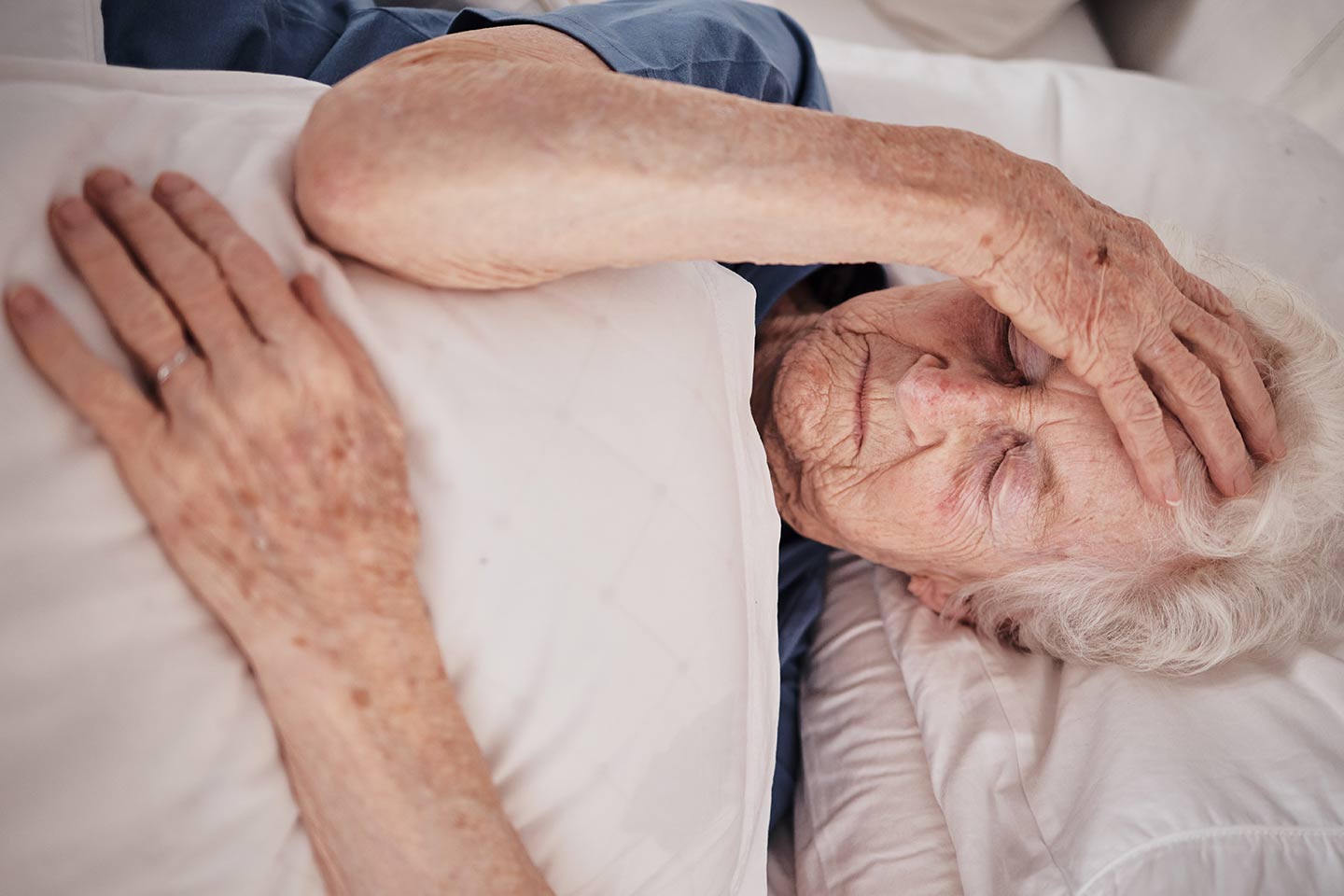 Photo of a woman lying in bed with her hand on her forehead