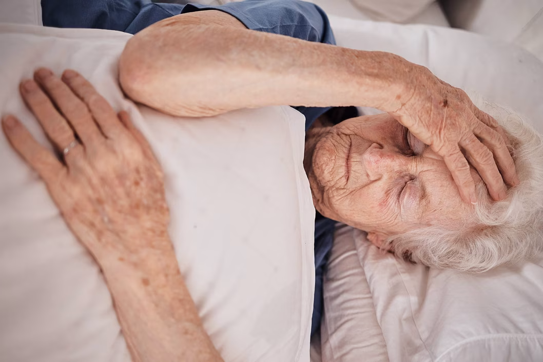 Photo of a woman lying in bed with her hand on her forehead