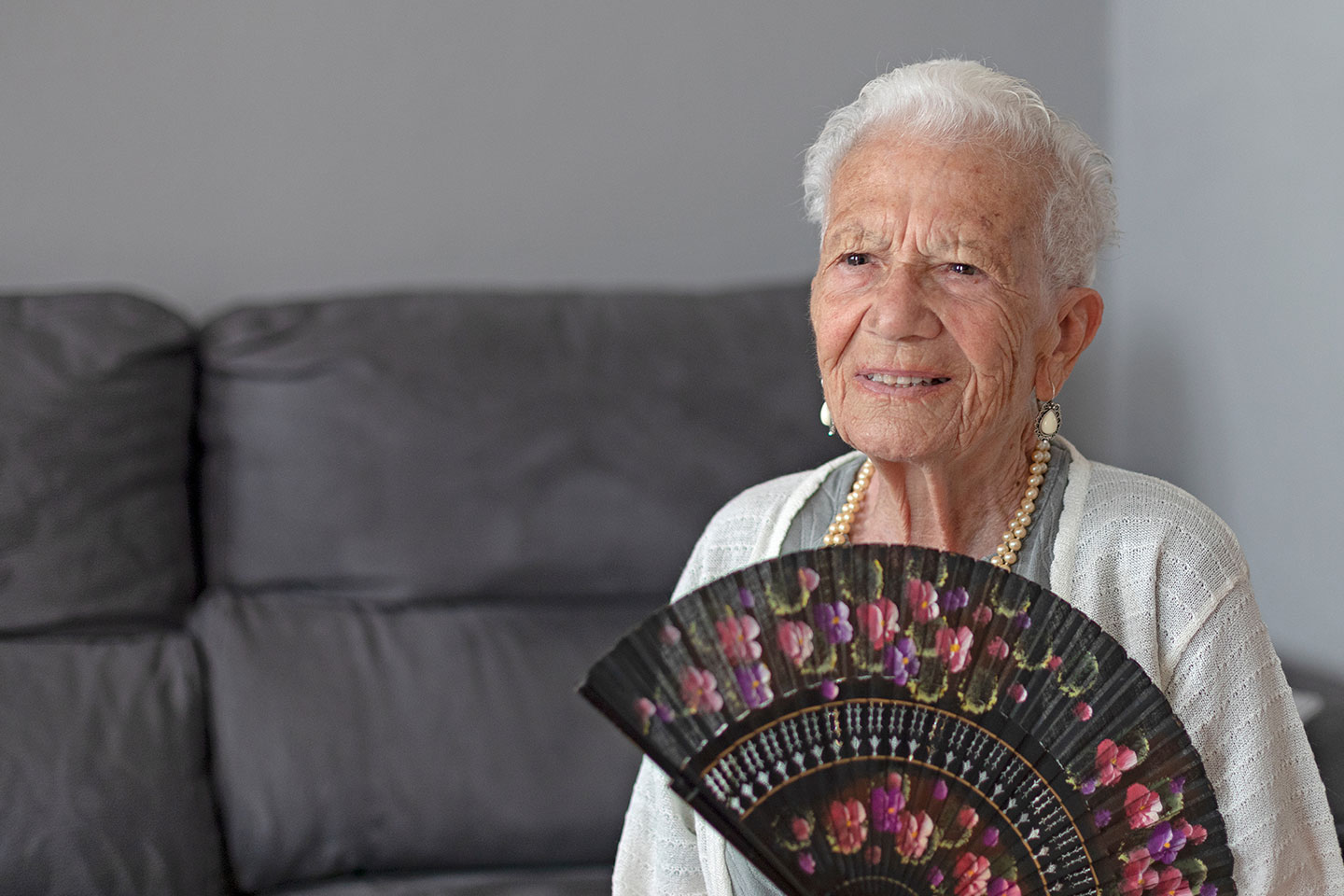 Photo of a person wearing matching pearls and holding a fan