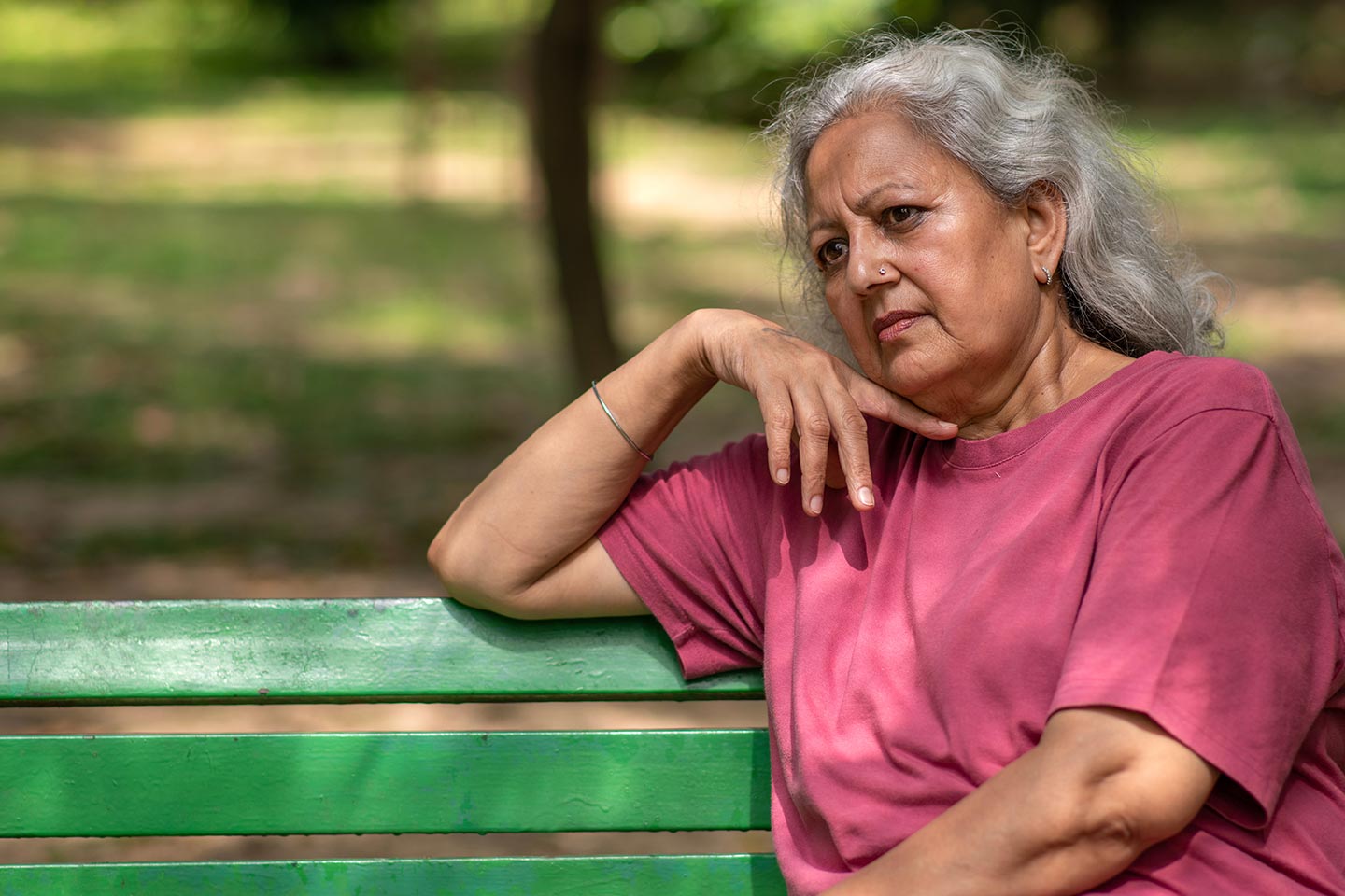 Photo of a woman in a raspberry t-shirt sitting on a green park bench