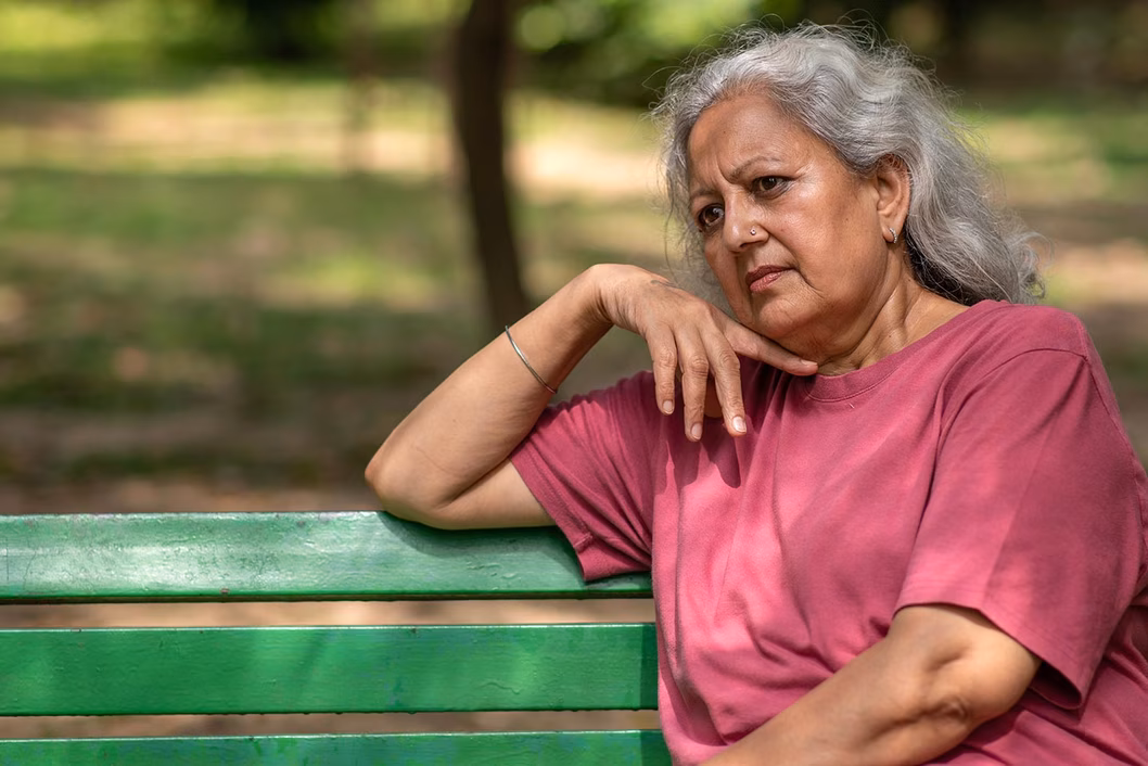 Photo of a woman in a raspberry t-shirt sitting on a green park bench