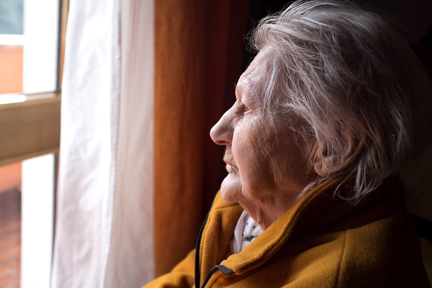 Photo of a woman in a mustard jacket looking out a window