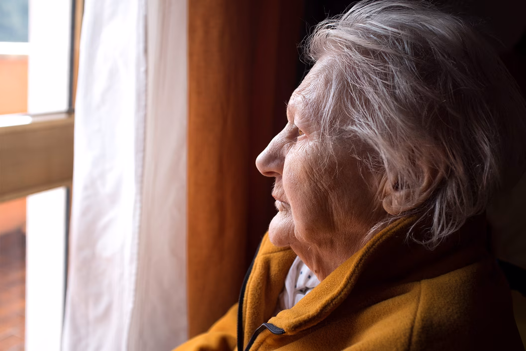 Photo of a woman in a mustard jacket looking out a window