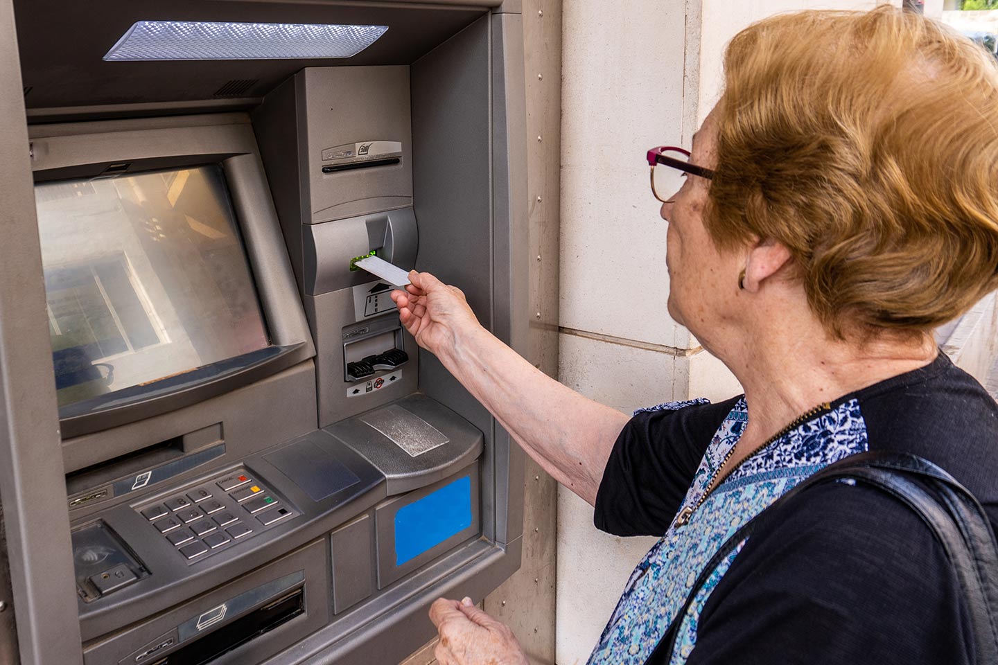 Image of an older woman inserting her card at an ATM
