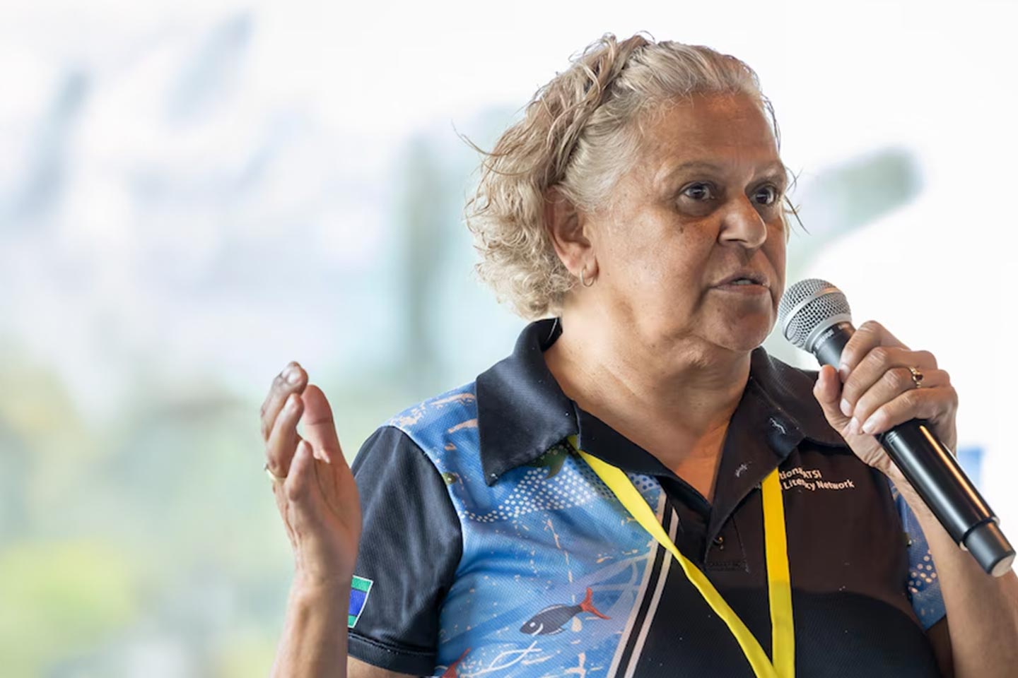 Photo of a woman with a yellow lanyard speaking into a microphone