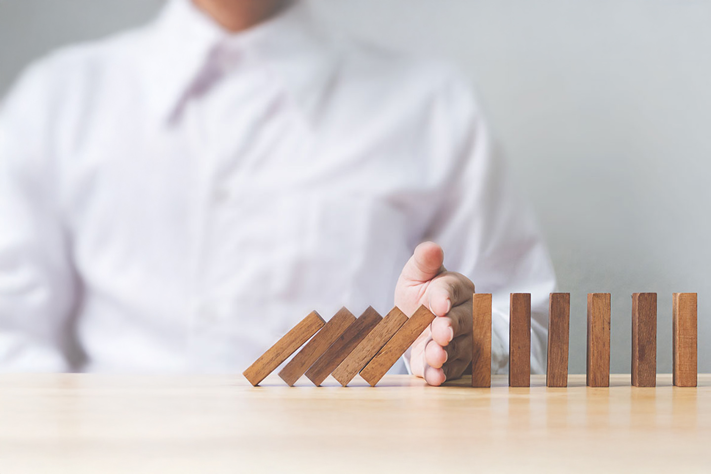 Photo of a hand preventing a row of dominoes falling