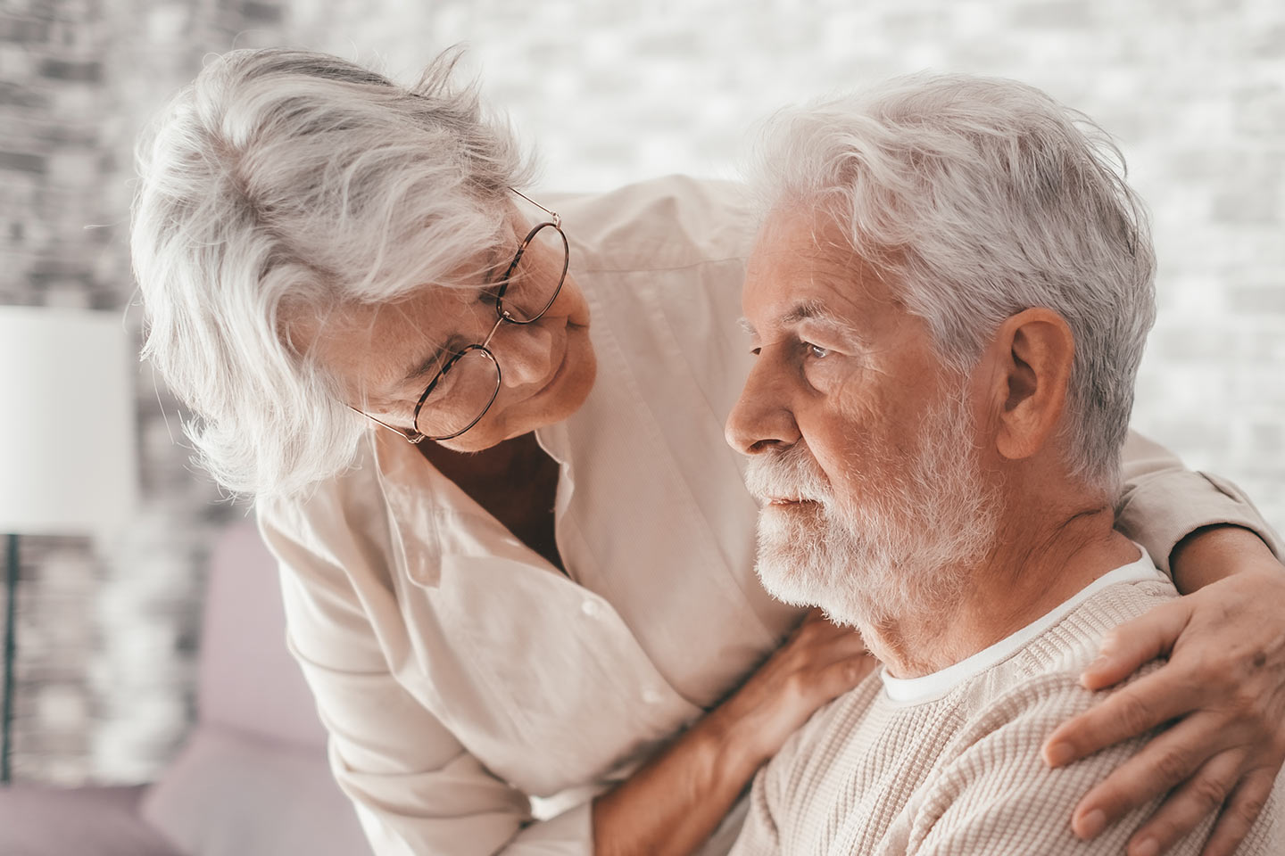 Photo of a woman in white embracing the shoulders of a man in cream