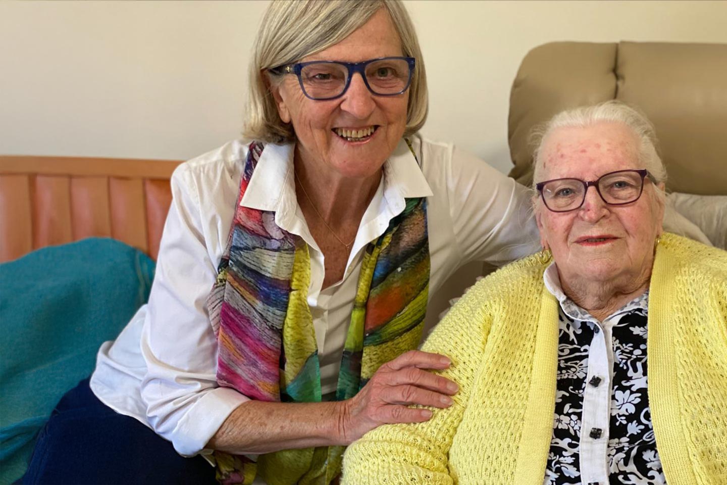 Photo of a woman with a colourful scarf embracing another in a yellow cardigan