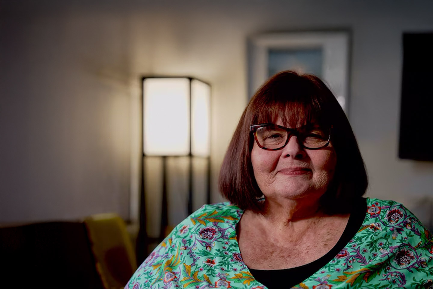 Photo of a woman in a paisley teal top in a cosy room