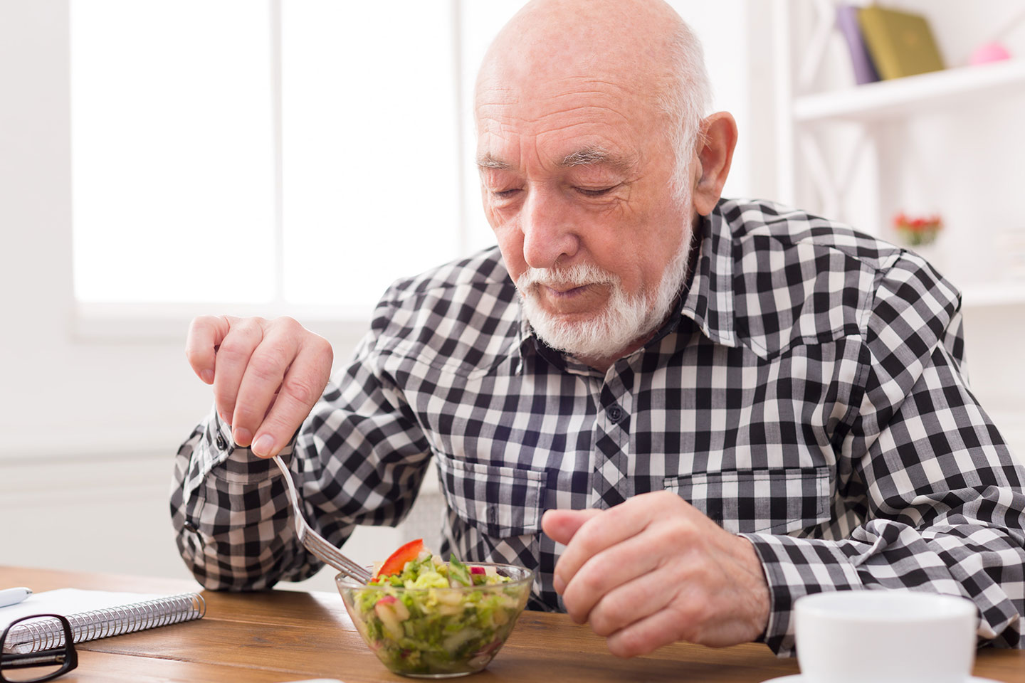 Older, balding man sitting at a table eating a small leafy salad