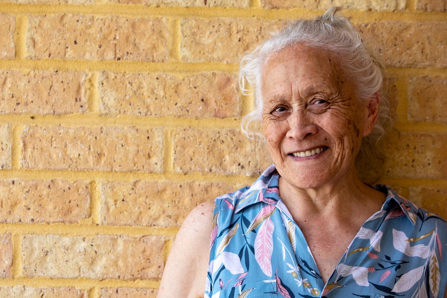 Photo of a smiling woman with a cream brick wall in the background