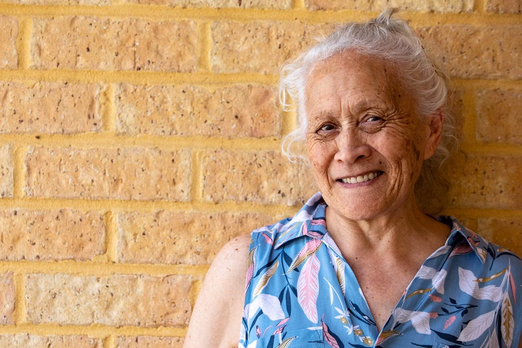 Photo of a smiling woman with a cream brick wall in the background