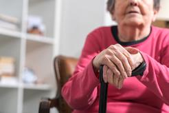 Image of an older woman's hands resting on a walking stick