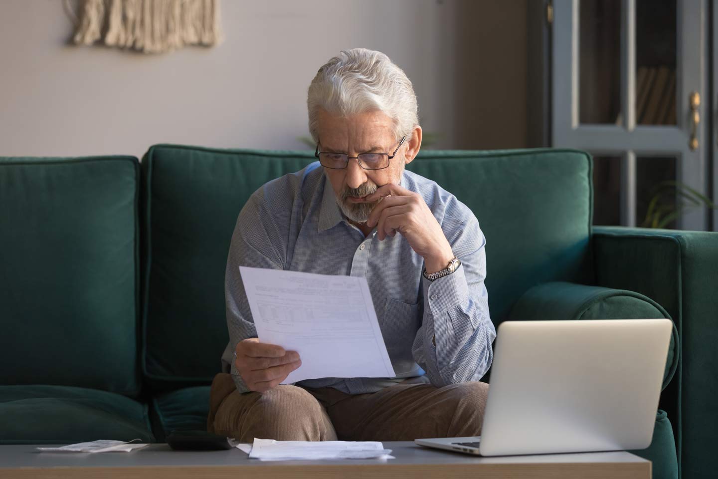 Senior man reading paperwork in front of an open laptop
