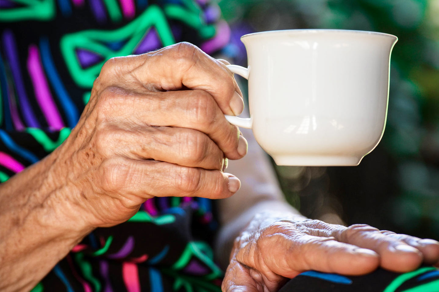 Photo of a senior hand holding a white tea cup