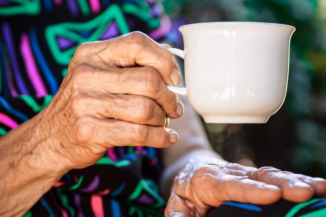 Photo of a senior hand holding a white tea cup
