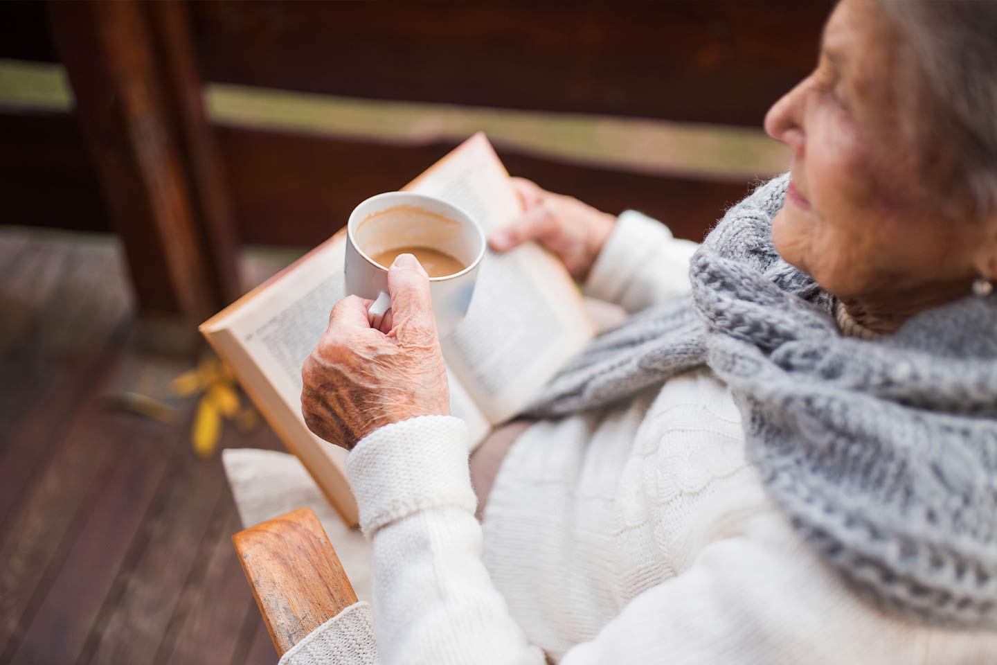 Photo of a seated woman with a cuppa and a book in her lap