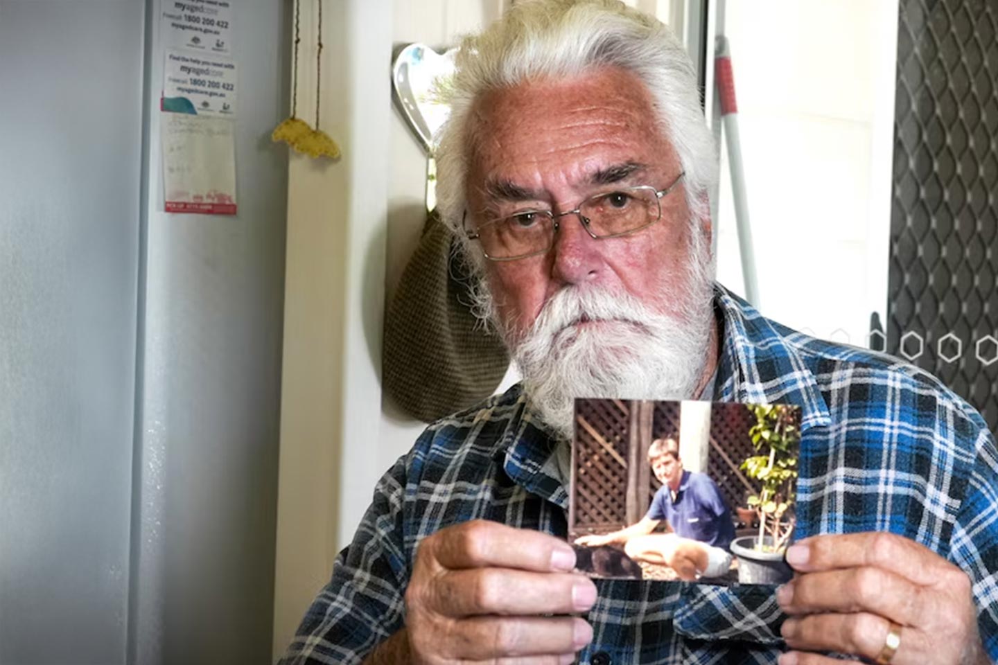 Photo of a white bearded man man holding up a photo