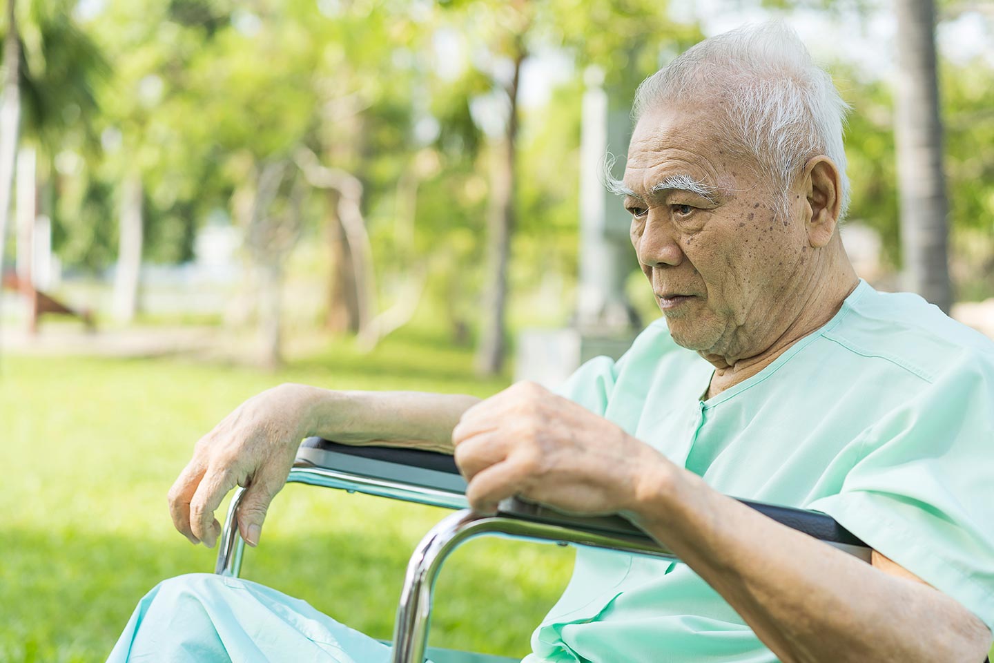 Photo of a man outdoors in a wheelchair wearing green hospital pyjamas