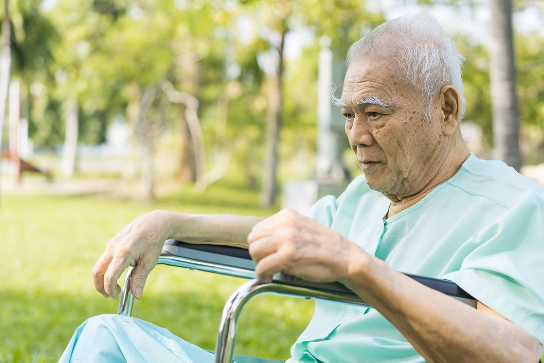 Photo of a man outdoors in a wheelchair wearing green hospital pyjamas