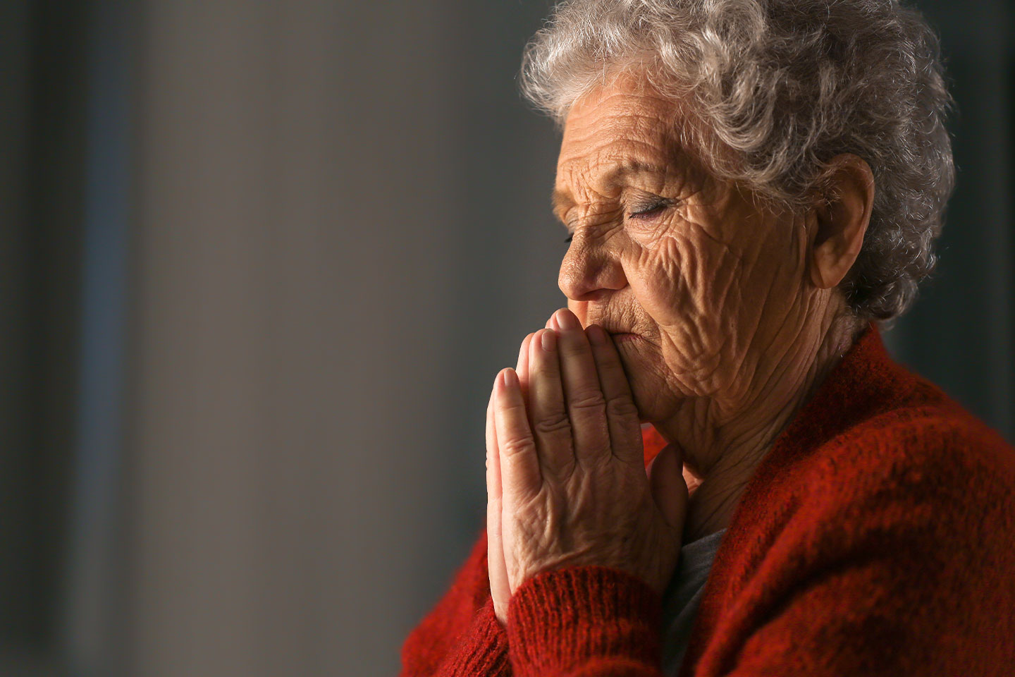 Photo of a woman praying in a red cardigan