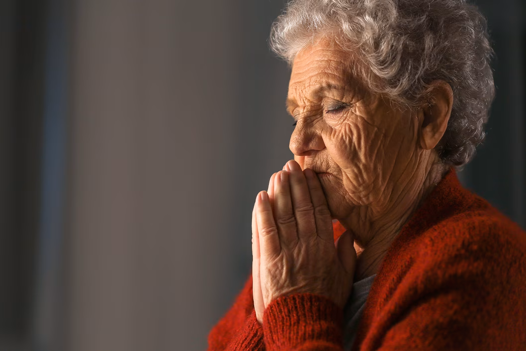 Photo of a woman praying in a red cardigan