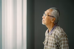 Older Asian man looking out a window