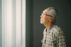 Older Asian man looking out a window