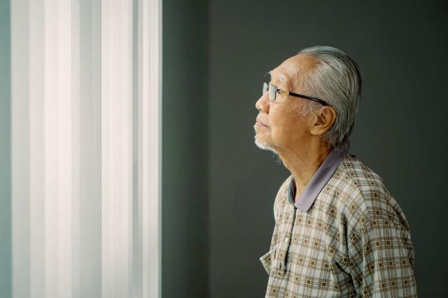 Older Asian man looking out a window