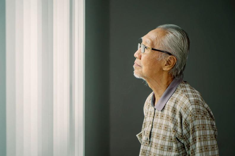Older Asian man looking out a window