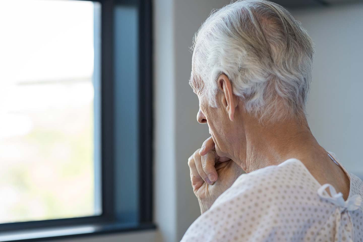 Photo of a man in a hospital gown staring out a window