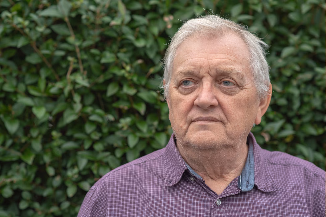 Photo of a man in a purple shirt in front of a hedge