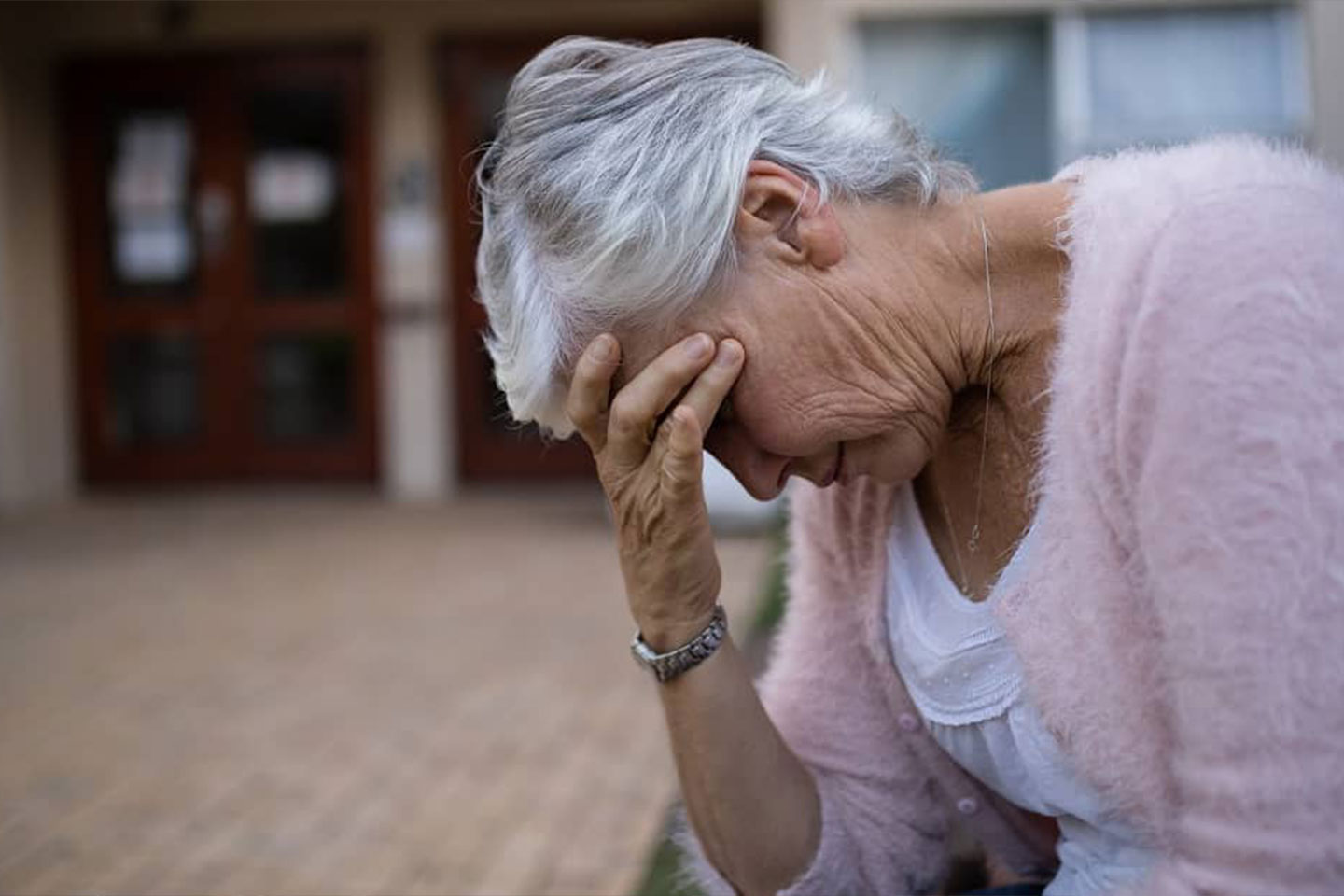 Photo of s woman in a pale pink cardigan with her head in her hands