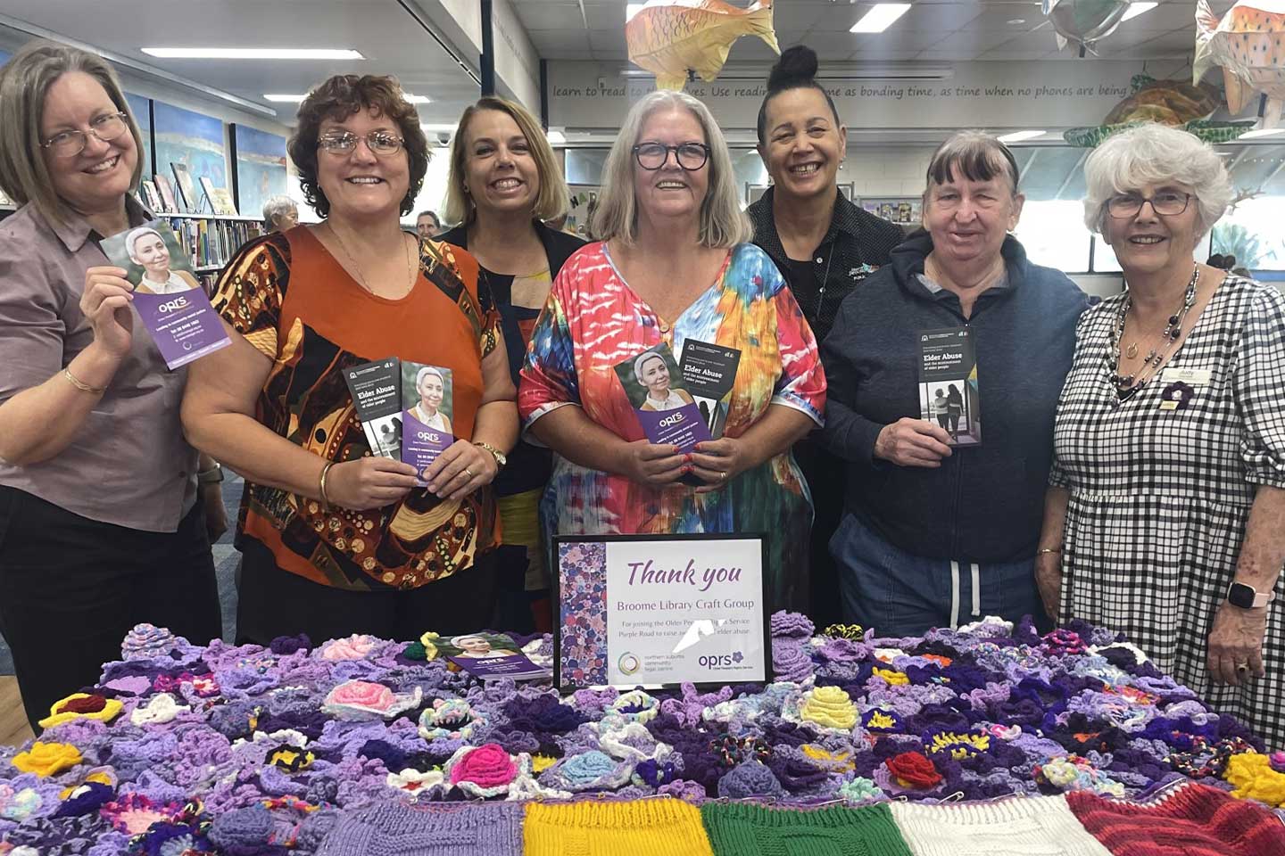 Photo of a group of smiling women standing behind a purple blanket