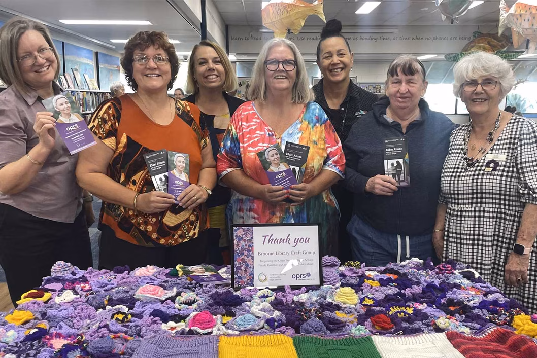 Photo of a group of smiling women standing behind a purple blanket