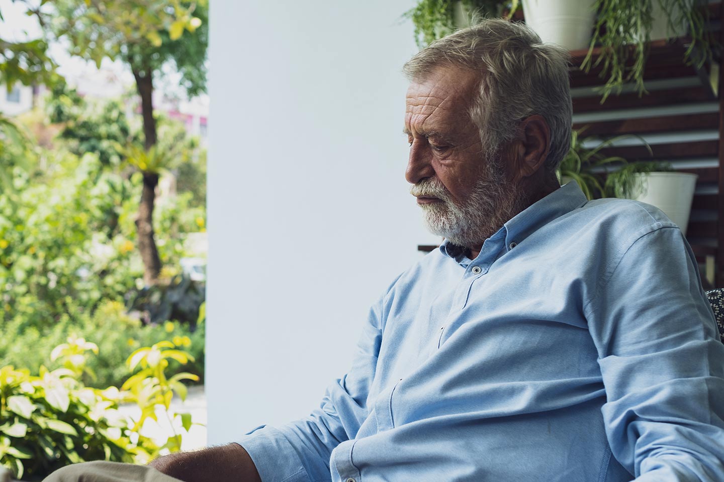 Photo of sad man with a white beard sitting near a garden