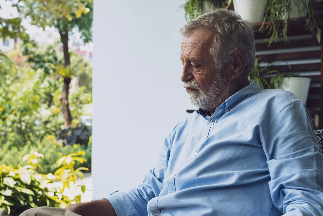 Photo of sad man with a white beard sitting near a garden