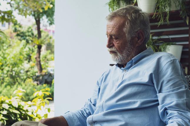 Photo of sad man with a white beard sitting near a garden