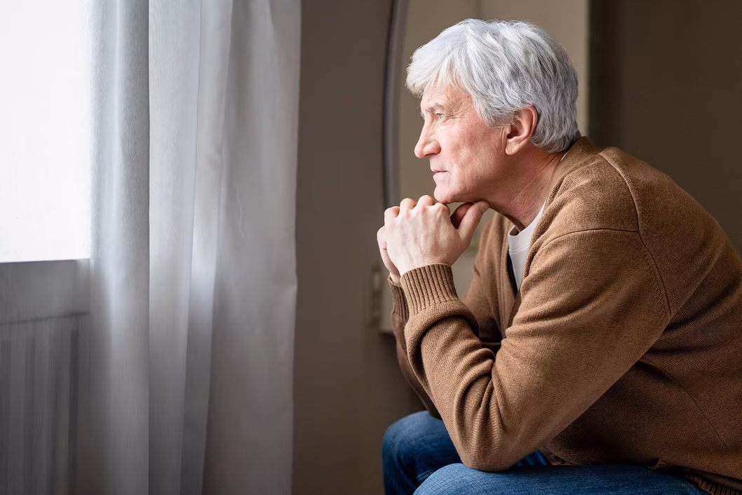 Photo of a man looking out a window with his chin on his hands