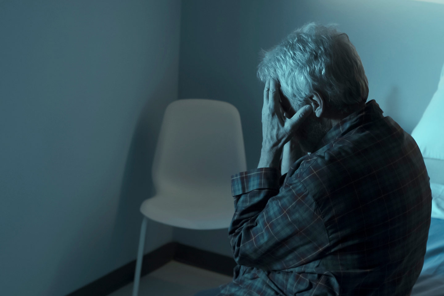 Photo of a person sitting in a dim room with head in hands
