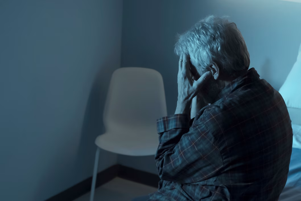 Photo of a person sitting in a dim room with head in hands