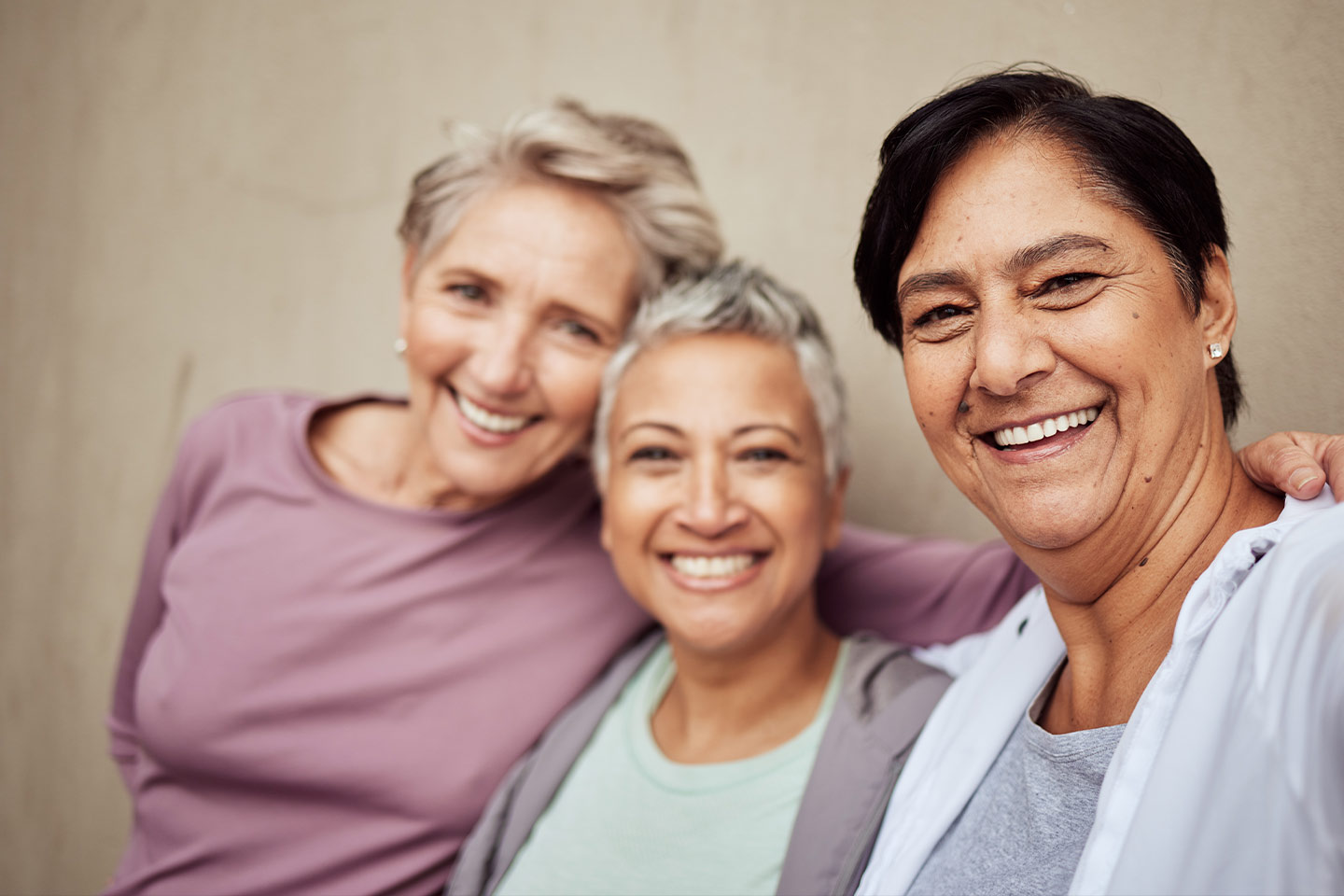 Photo of three smiling women wearing soft pinks and grey