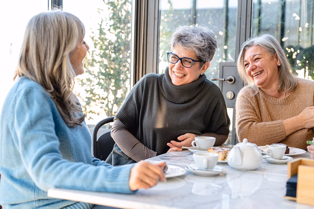 Photo of three women enjoying a laugh over tea and cake