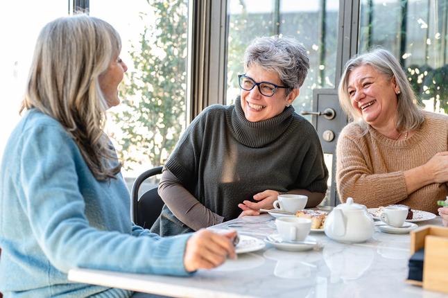Foto von drei Frauen, die sich bei Tee und Kuchen amüsieren