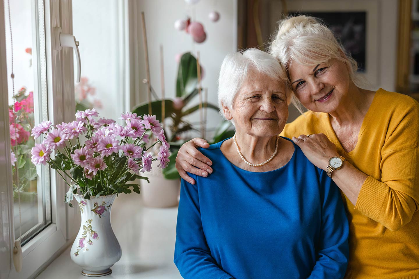 Photo of two smiling women with a vase of pink flowers
