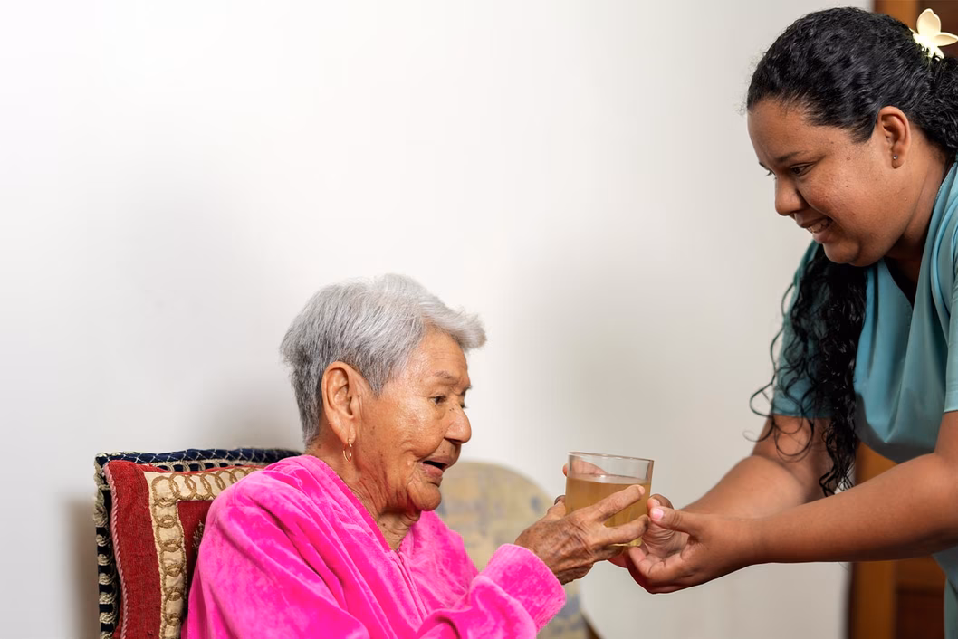 Photo of a woman giving a senior lady something to drink