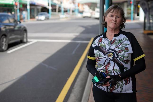 Photo of a woman in cycling gear standing by a city street