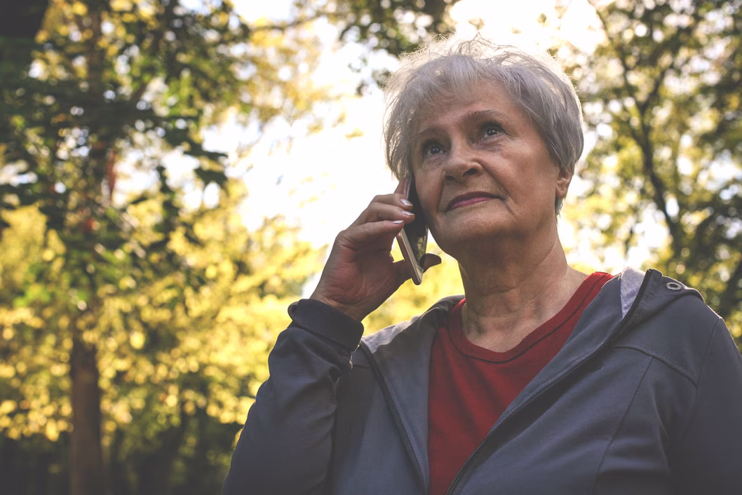 Image of an older woman who is outside and holding a smartphone to her ear.