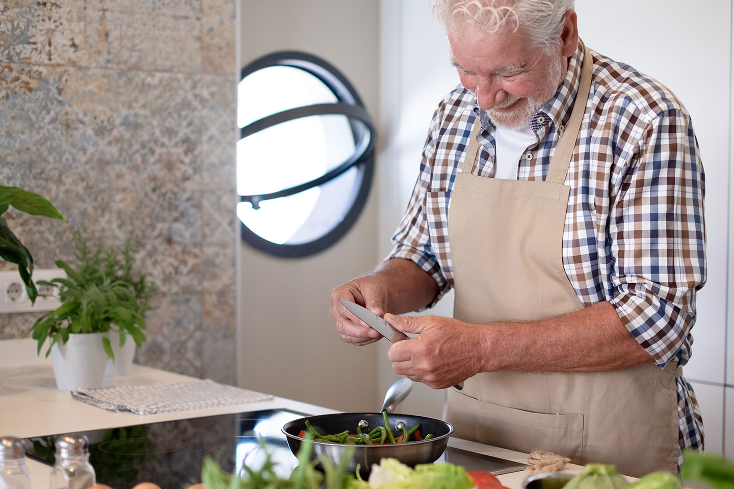 Photo of a man in an apron peeling veggies in a kitchen